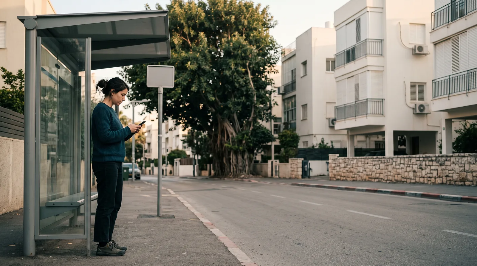 A woman at a quiet city bus stop, reading a message on her phone